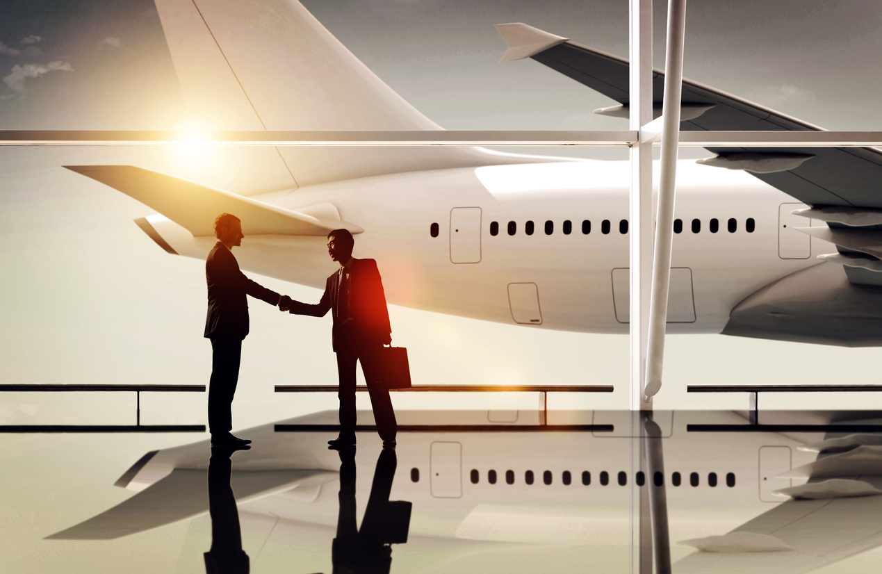 Business partners shaking hands in front of a plane